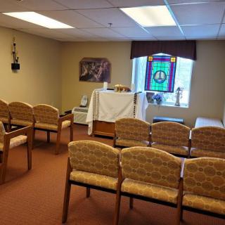 A small chapel with chairs arranged in rows facing an altar, featuring a stained glass window.