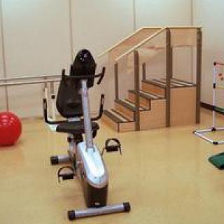 A physical therapy room featuring a recumbent exercise bike, stairs, and other rehabilitation equipment.