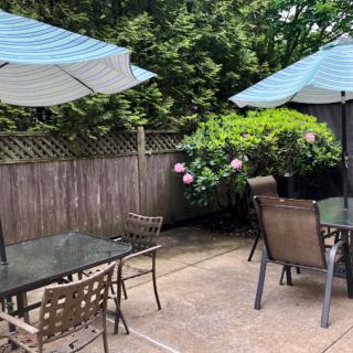 A cozy outdoor patio with tables, chairs, and umbrellas surrounded by greenery.