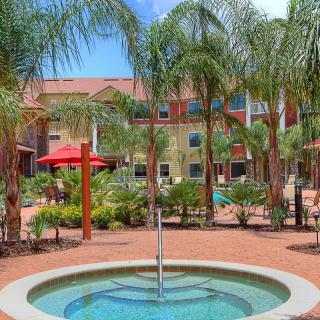 A serene outdoor garden area with a small fountain surrounded by palm trees and hotel buildings.