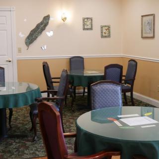 A cozy dining room with round tables covered in green tablecloths and surrounded by comfortable chairs.