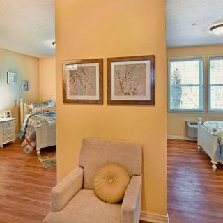 A cozy interior space featuring a chair, two bedrooms with beds, and artwork on yellow walls.