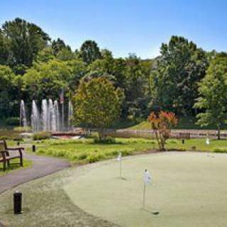 A scenic view of a golf course featuring a putting green and fountains amidst lush greenery.