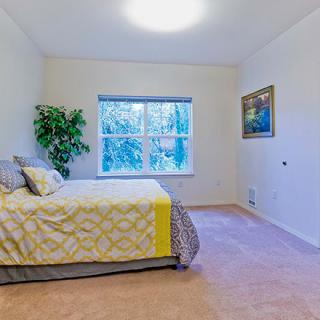 A bright and airy bedroom with a neatly made bed, large window, and tasteful decor.