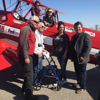A group of individuals poses for a photo beside a red biplane, capturing a moment of joy and camaraderie.