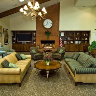 A cozy and well-decorated living room featuring sofas, a central coffee table, a fireplace with a clock above it, and built-in bookshelves.