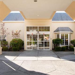 The image shows the entrance of a building with glass doors, featuring surrounding landscaping and architectural details.