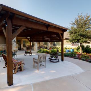 A wooden pergola with outdoor seating, surrounded by a landscaped garden.