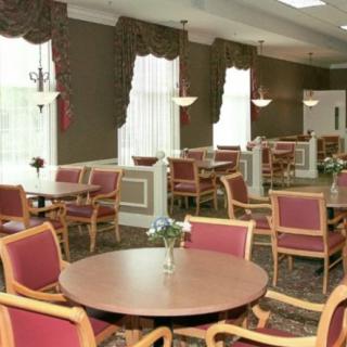 A well-lit dining area with several round tables and chairs arranged neatly by large windows adorned with curtains.
