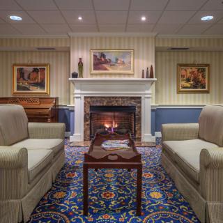 A cozy living room with a traditional fireplace, surrounded by sofas and decorated with artwork and a patterned carpet.