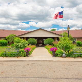 A welcoming entrance to a building adorned with colorful flowers and an American flag under a cloudy sky.
