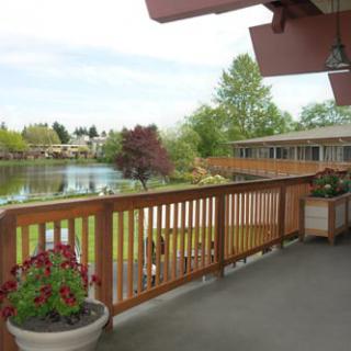 A balcony overlooking a serene lake with potted flowers and wooden fencing.