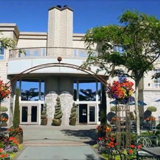 A beautifully landscaped building entrance with trees and colorful flowers under a clear blue sky.