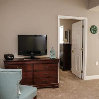 A cozy bedroom with a TV on a wooden dresser and an open door leading to another room.