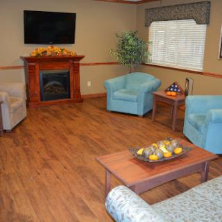A cozy living room featuring blue chairs, a wooden fireplace, and a TV mounted on the wall.