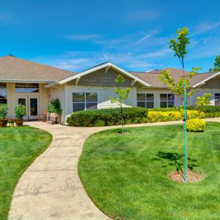 A well-maintained residential house with a lush green lawn and a curved pathway leading to the entrance on a sunny day.