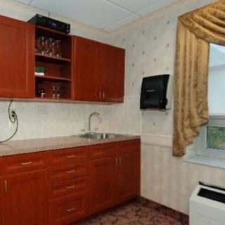A small kitchen area with wooden cabinets, a sink, and a window with curtains.