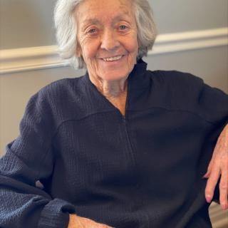 An elderly woman smiling while sitting indoors.