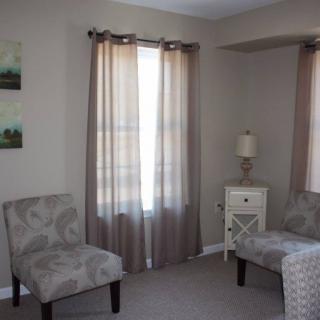 A cozy living room with two chairs, a side table, and soft curtains.