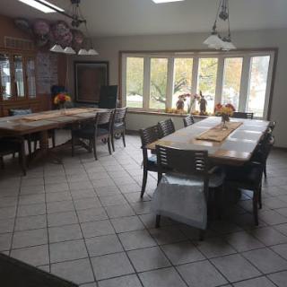 A spacious dining area with long tables and chairs, illuminated by large windows and overhead lights.