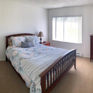 A cozy bedroom featuring a wooden bed with patterned bedding, a bedside lamp, and a window with blinds.