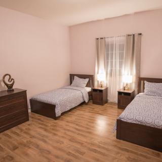 A cozy bedroom with two single beds, wooden flooring, and warm lighting from bedside lamps.