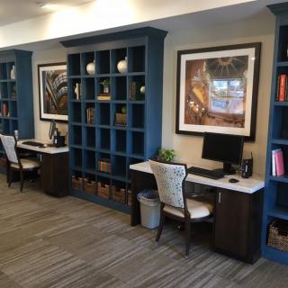 A modern office workspace featuring built-in shelves, two desks with computers, and elegant chairs.