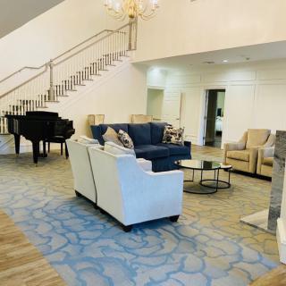 A spacious living room with elegant furniture and a grand piano near a staircase.