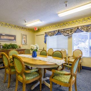 A cozy dining room with a classic wooden table and ornate chairs, adorned with a vase on the table and elegant curtains over the windows.