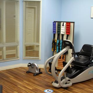 A small gym room with exercise equipment, mirrors, and karate belts on display.