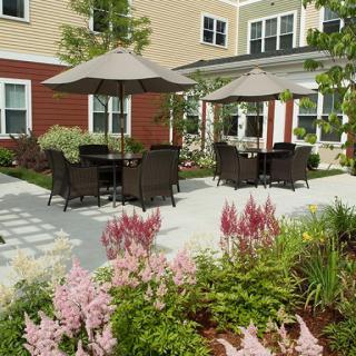 A beautifully landscaped garden patio with outdoor seating and umbrellas, adjacent to a residential building.