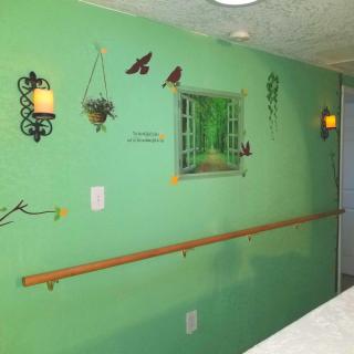 A green wall decorated with a mural featuring an open window illusion, plants, and birds. The wall also includes sconces and a wooden handrail.