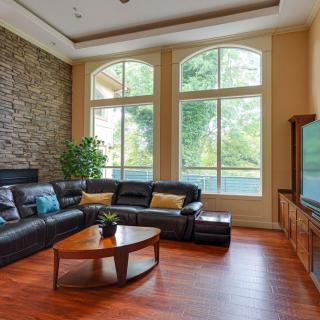 A modern living room with a leather sofa and large windows, featuring a stone accent wall and hardwood flooring.