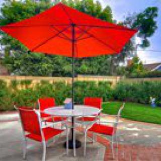 A cozy backyard patio setup with a red umbrella and matching chairs around a round table.