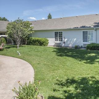 A backyard with a well-maintained lawn and garden, featuring a concrete pathway and surrounding greenery.