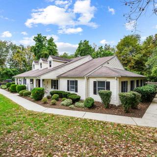 A quaint single-story house surrounded by trees and greenery on a clear day.