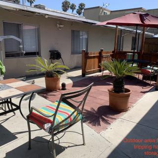 A sunny residential patio with chairs, potted plants, and a large umbrella.