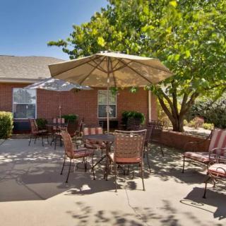 A sunny patio area with outdoor seating and umbrella, surrounded by greenery.