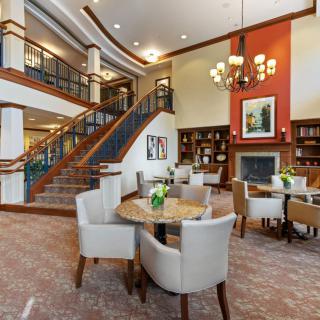 A spacious and elegantly designed lobby featuring a staircase, chandelier, and comfortable seating area with tables and chairs.