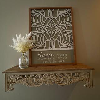 A beautifully arranged wooden shelf featuring intricate wall art and a vase of flowers.