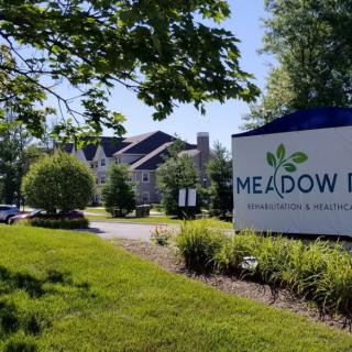 A sunny view of a building with a 'Meadow' sign surrounded by lush greenery.