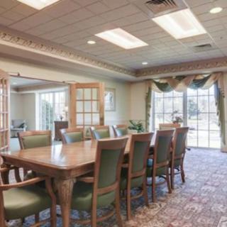 A spacious dining or conference room with a large table and chairs, featuring large windows with curtains and carpeted flooring.