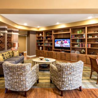 A cozy living room with a television, comfortable seating, and well-organized shelves.