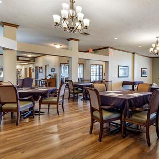 A spacious dining area with wooden flooring, elegant chandeliers, and neatly arranged tables and chairs.