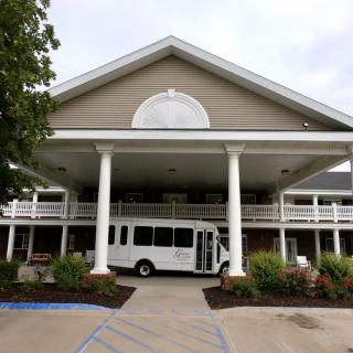 A large building entrance with columns and a white bus parked in front.