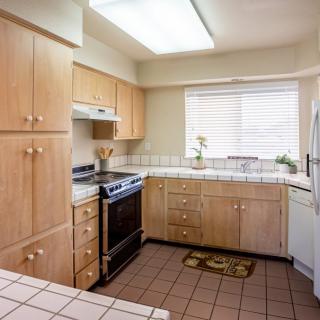 A kitchen with wooden cabinets, a stove and oven, and a tiled floor.