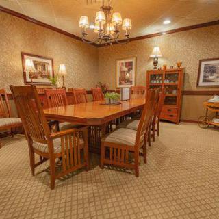 A cozy dining room with wooden furniture and a chandelier, featuring a carpeted floor and wall paintings.