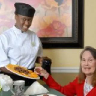 A chef serves food to a smiling customer in a restaurant setting.