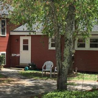 A suburban house with a red exterior, surrounded by trees and featuring a white plastic chair on the pathway.