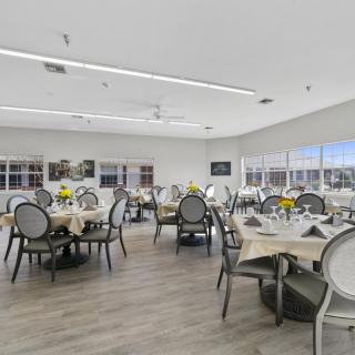 A spacious and well-lit dining area with neatly arranged tables and chairs, adorned with table settings and floral decorations.